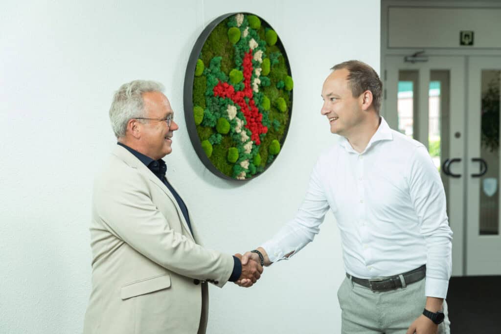 Two men in business attire shaking hands and smiling in an office
